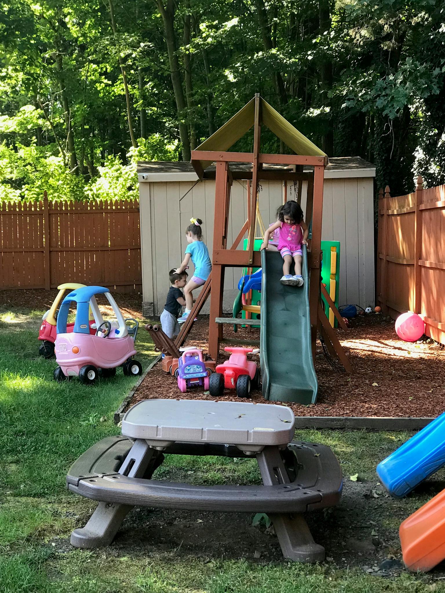Children playing on a slide and climbing structure in a backyard