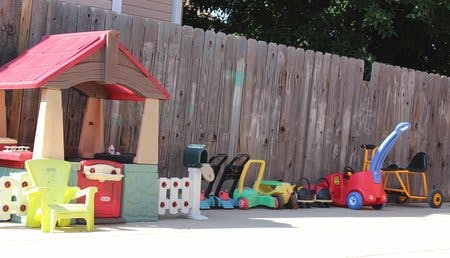Playhouse and various ride-on toys next to a wooden fence
