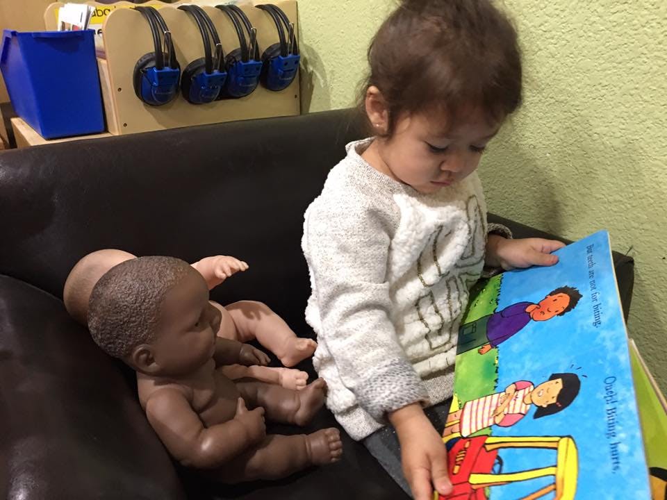 Child sitting on a couch with a doll, holding a book