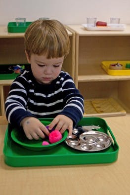 Child playing with pink modeling clay on a green tray