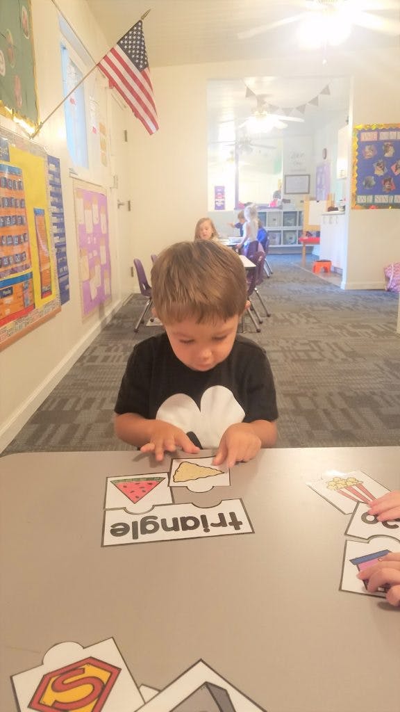 Child playing with puzzle pieces on a table in a classroom