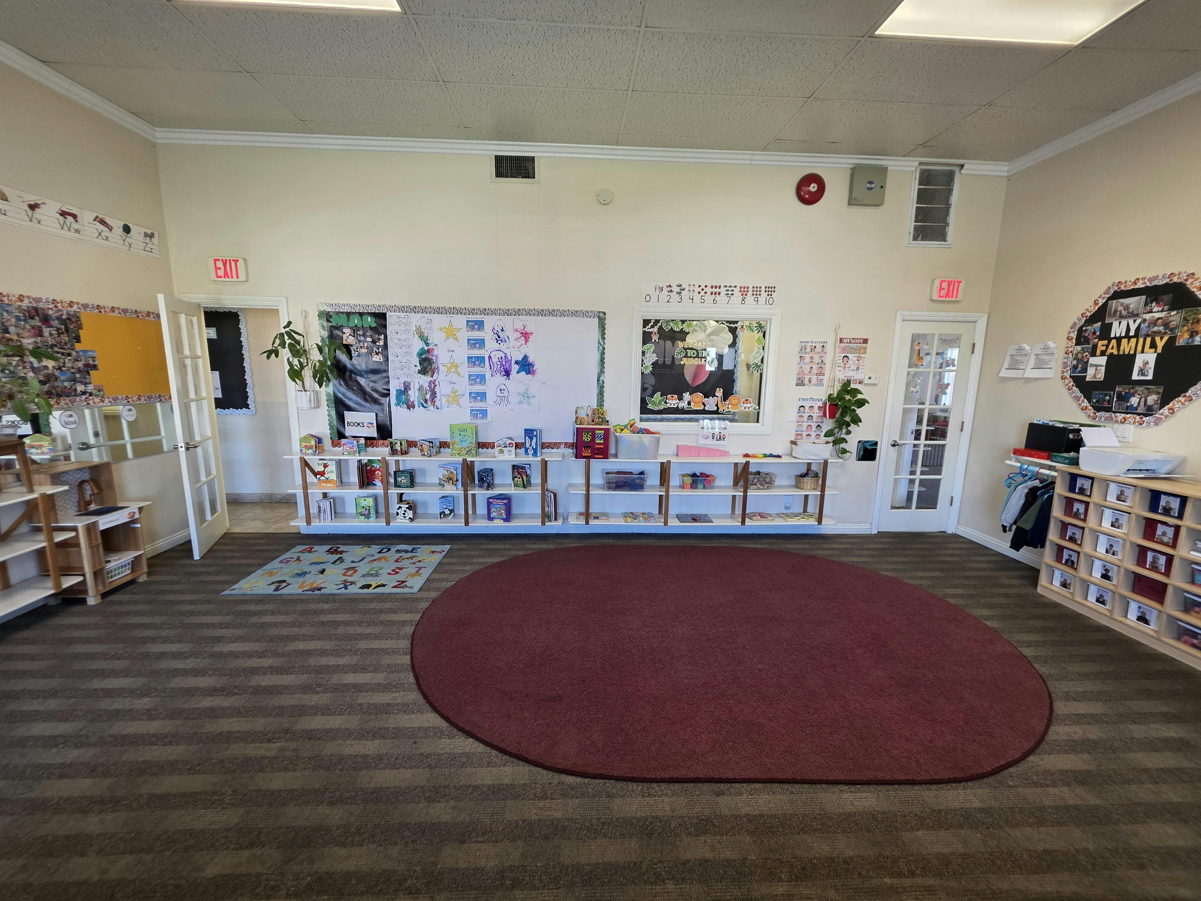Classroom with shelves of books and toys, several posters on the walls, and two rugs on the floor