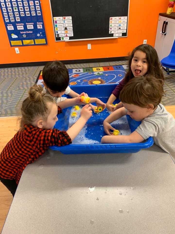 Four children playing with rubber ducks in a blue water table