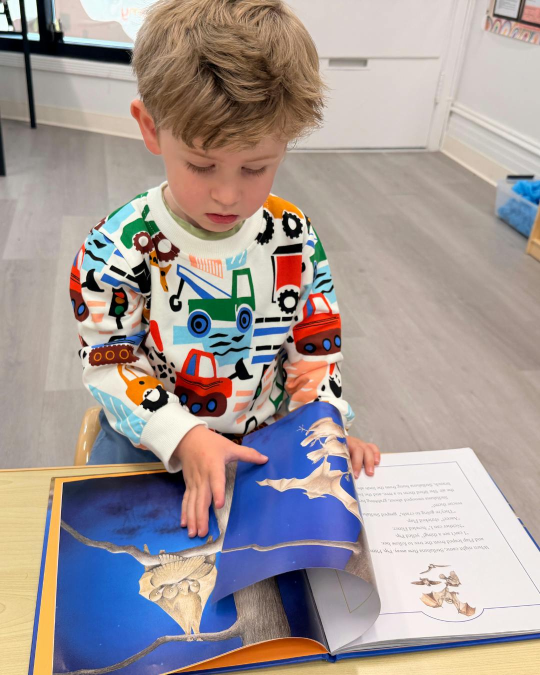 Child in a classroom looking down at an open book with bat illustrations