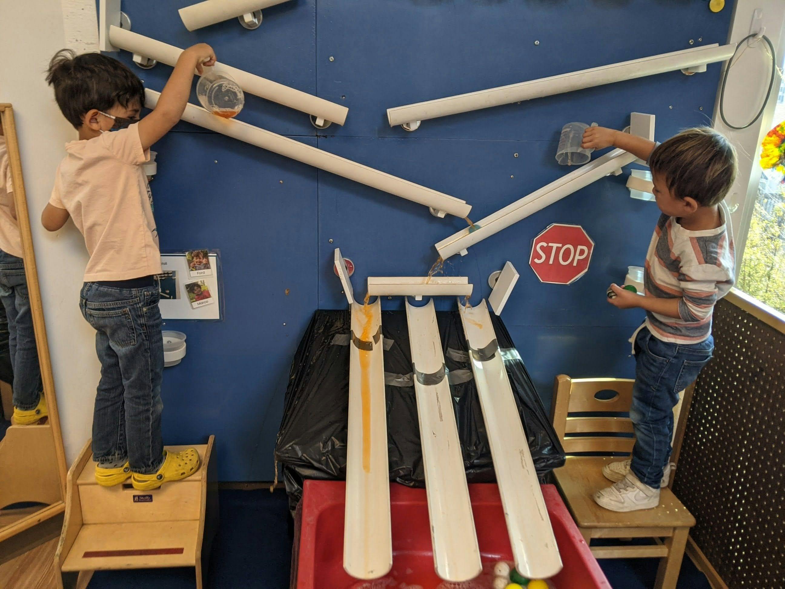 Two children playing with a ball run on a blue wall