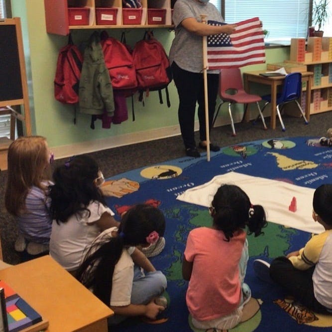Person holding an American flag in front of children sitting on a rug