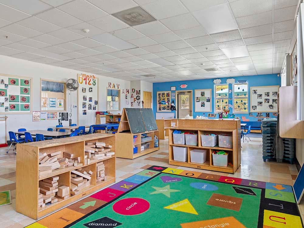 Classroom with child-sized tables, shelves with blocks and toys, and a colorful rug