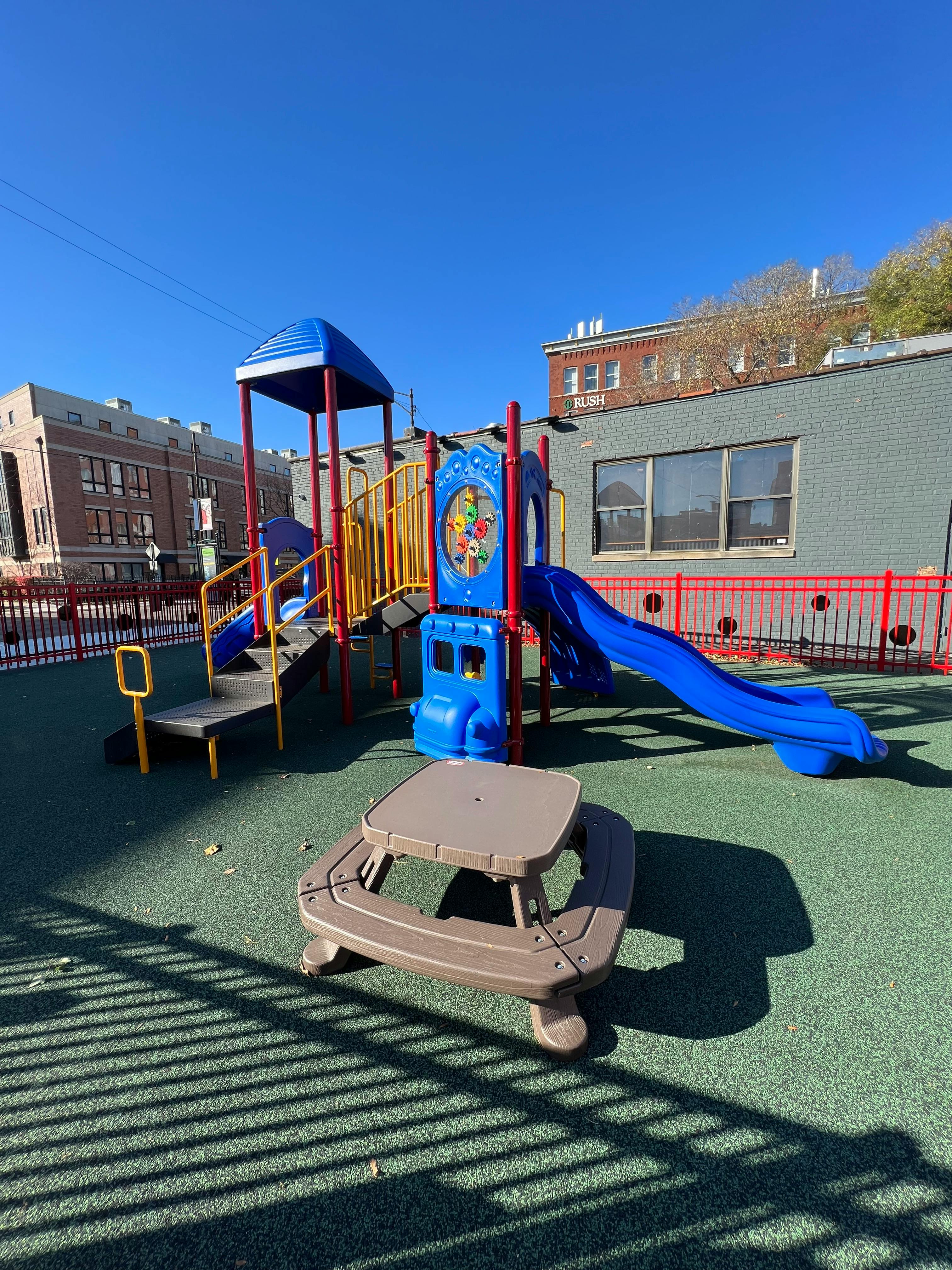 Playground with blue and yellow play structure and a brown picnic table