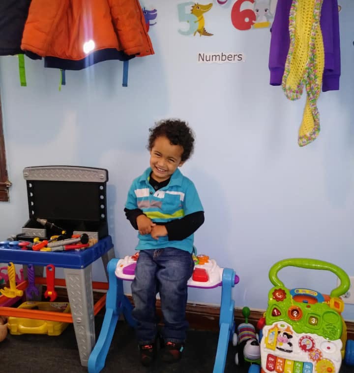 Child sitting on a toy piano in a room with a toy workbench