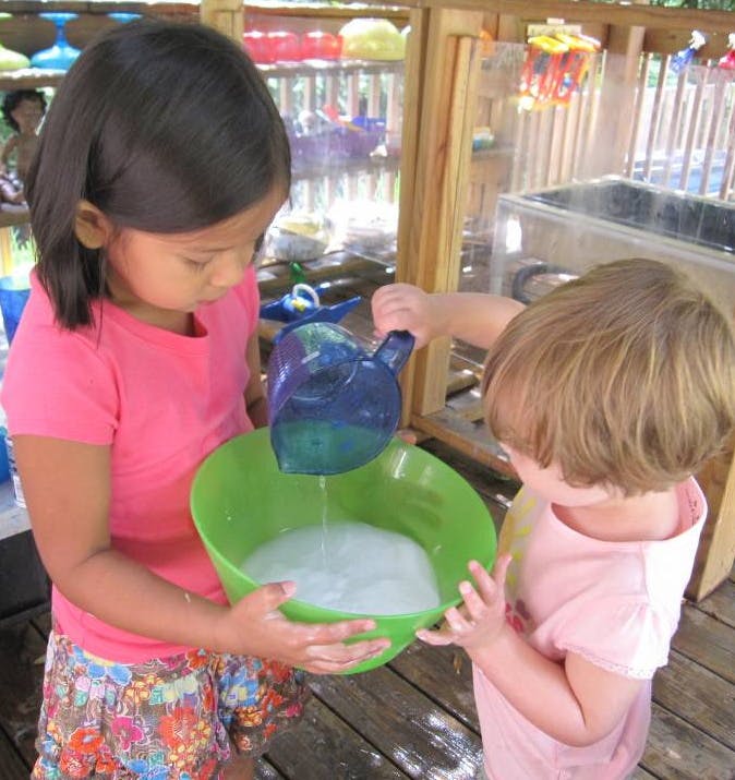 Two children pouring liquid from a pitcher into a bowl