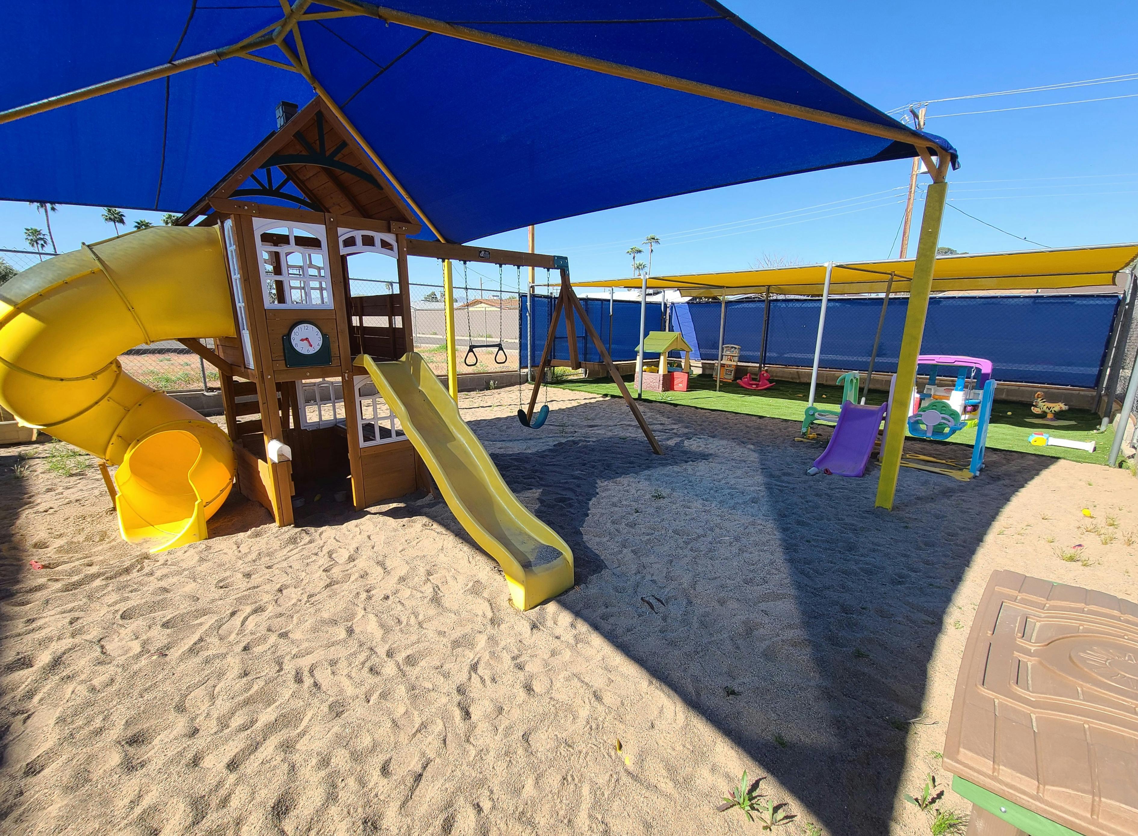 Playground with slides, swings, and sand under a blue shade structure