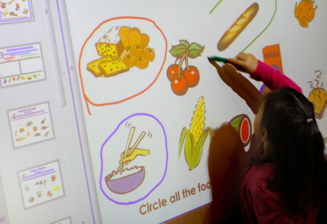 Child drawing on an interactive whiteboard with food illustrations