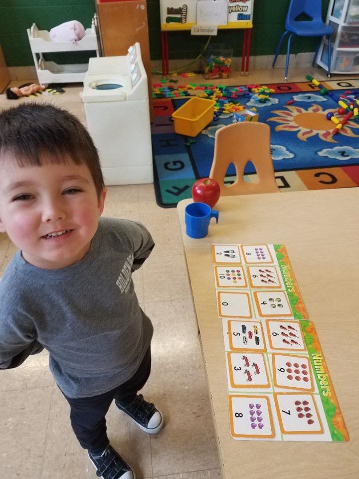Child standing next to a table with number cards in a classroom