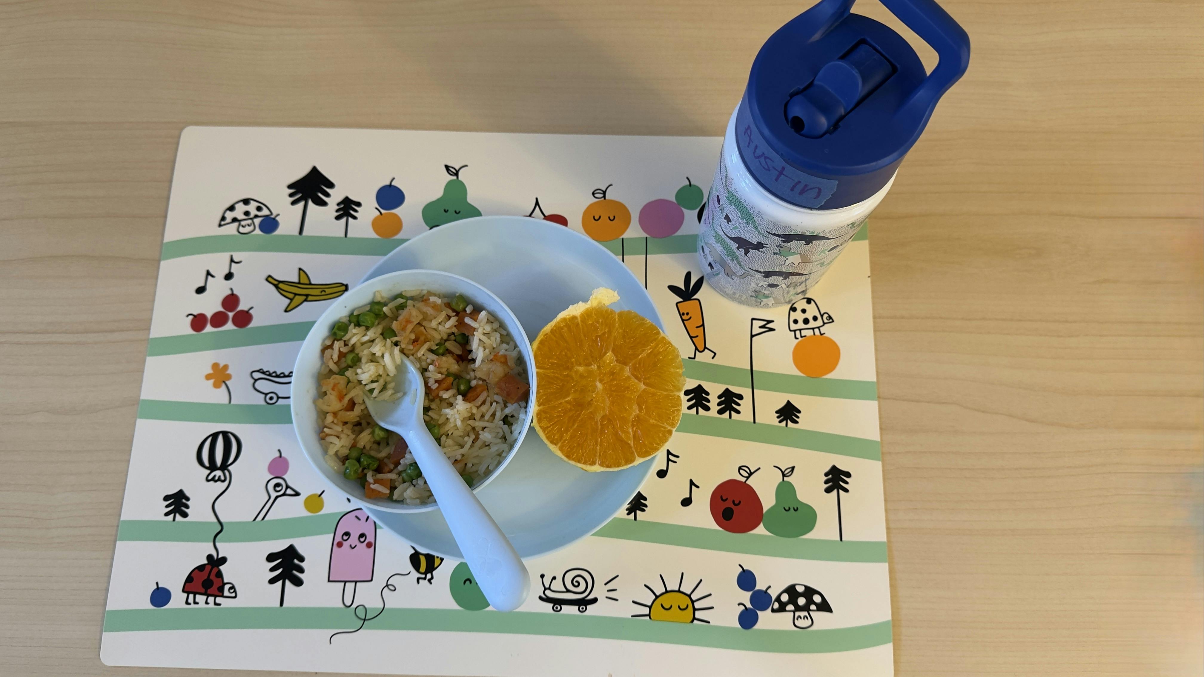 Bowl of food with a spoon, orange slice, and water bottle on a placemat