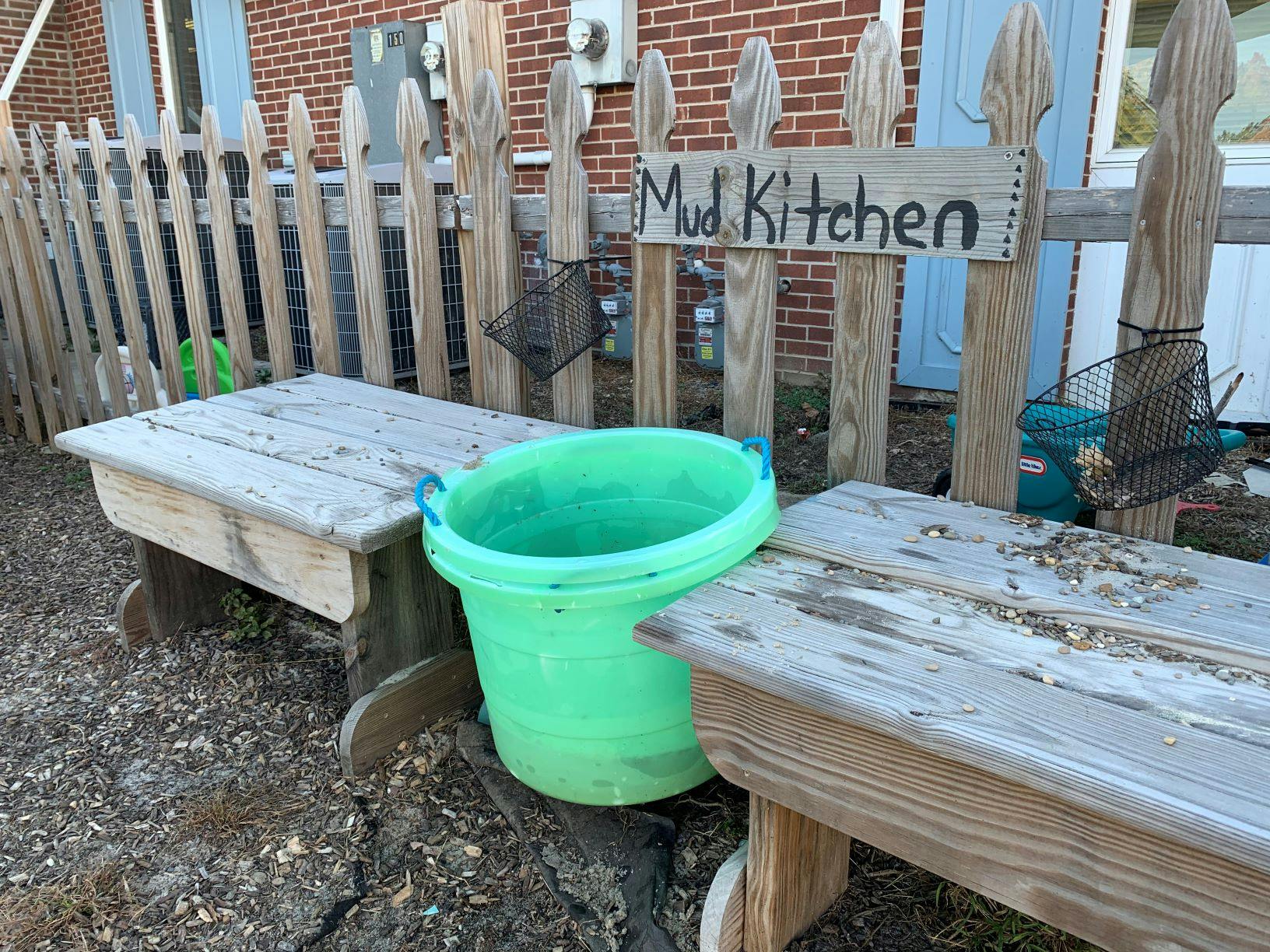 Mud Kitchen sign on a wooden fence with a green bucket and wooden tables