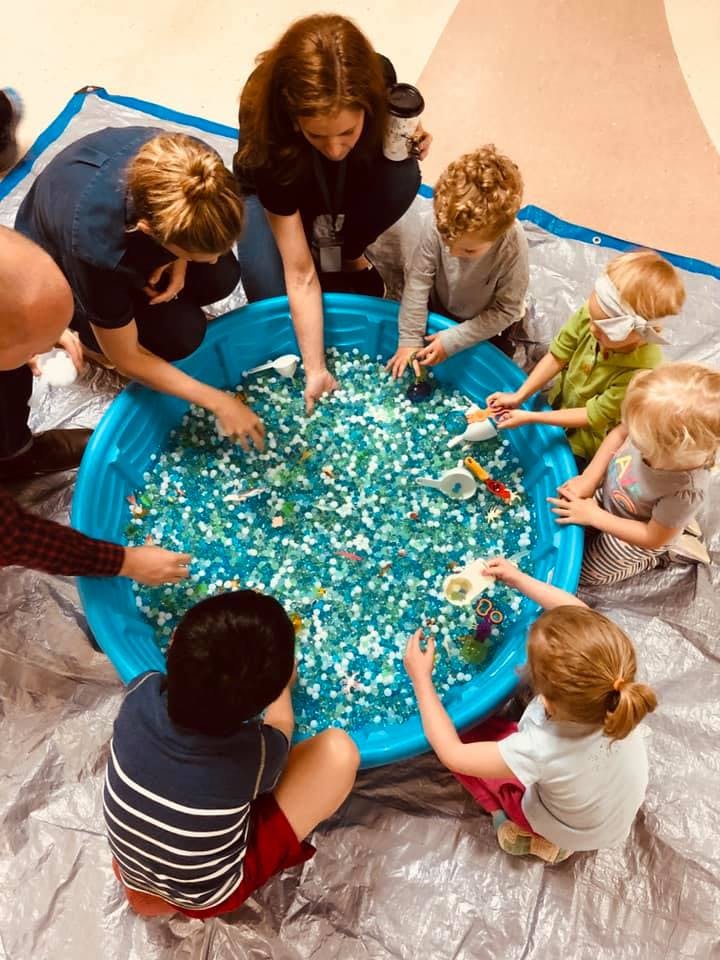 Adults and children playing in a blue sensory bin filled with small objects