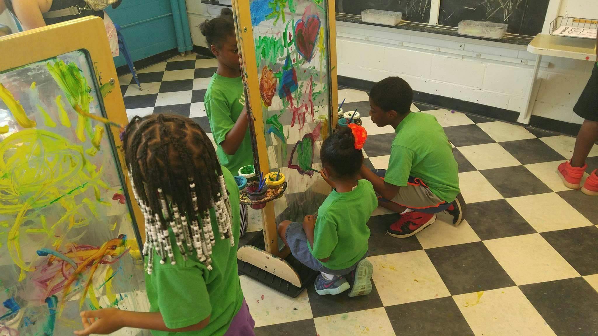 Children painting at easels in a room with a checkered floor