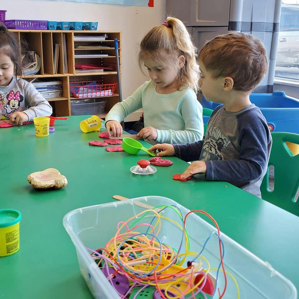 Three children playing with modeling clay at a green table