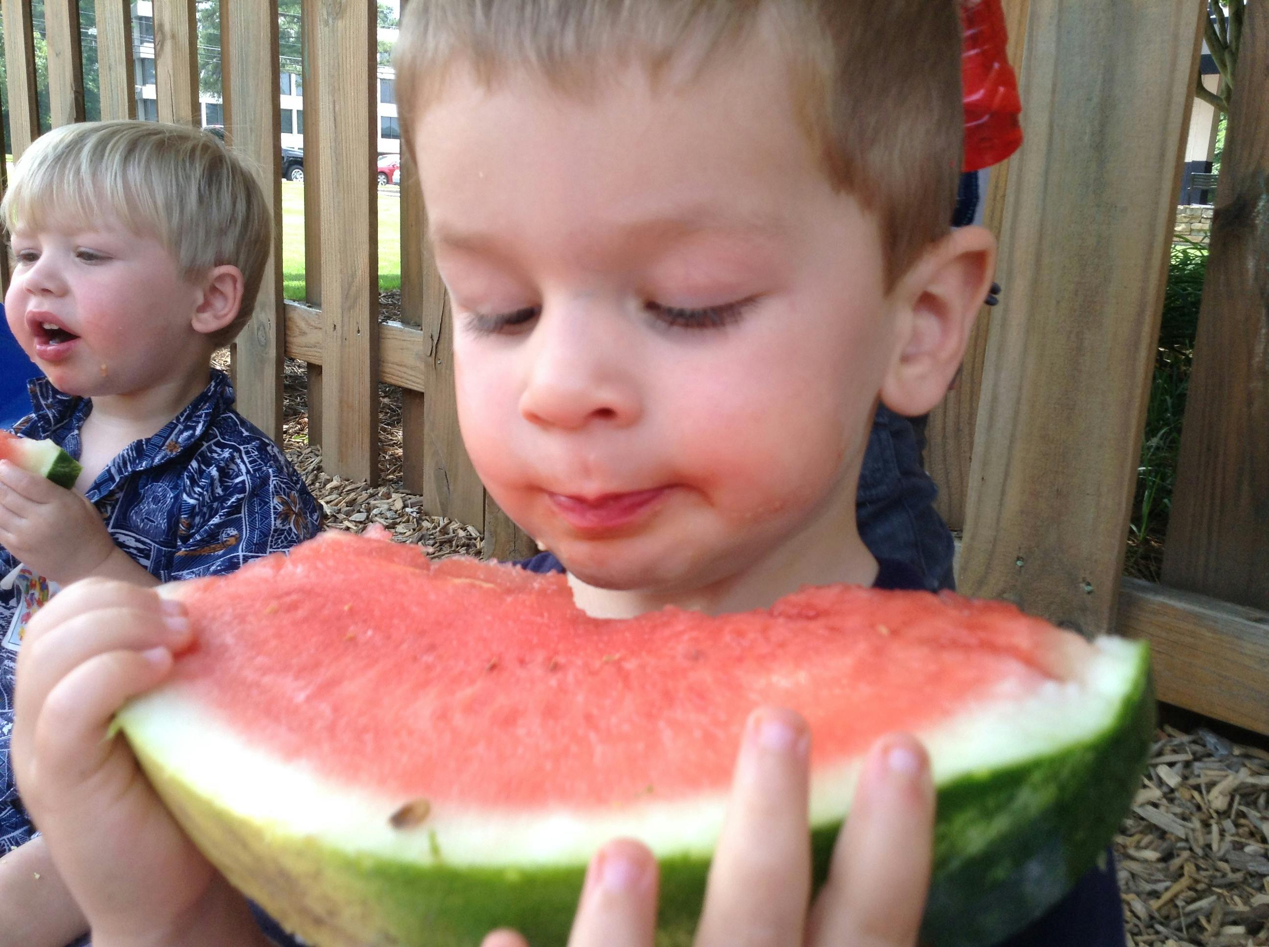 Two children eating large slices of watermelon outdoors