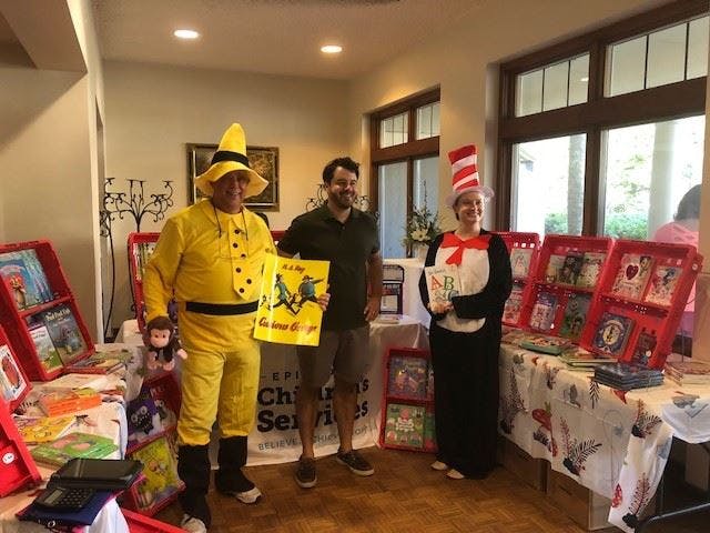 Three people in costumes standing by tables with books and displays