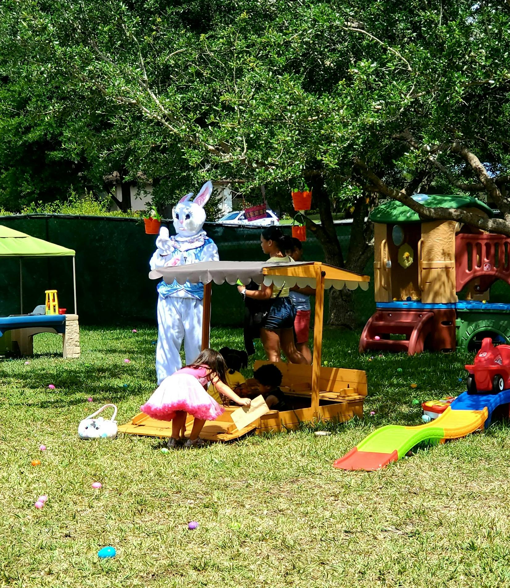 Person in bunny costume with children playing in a sandbox