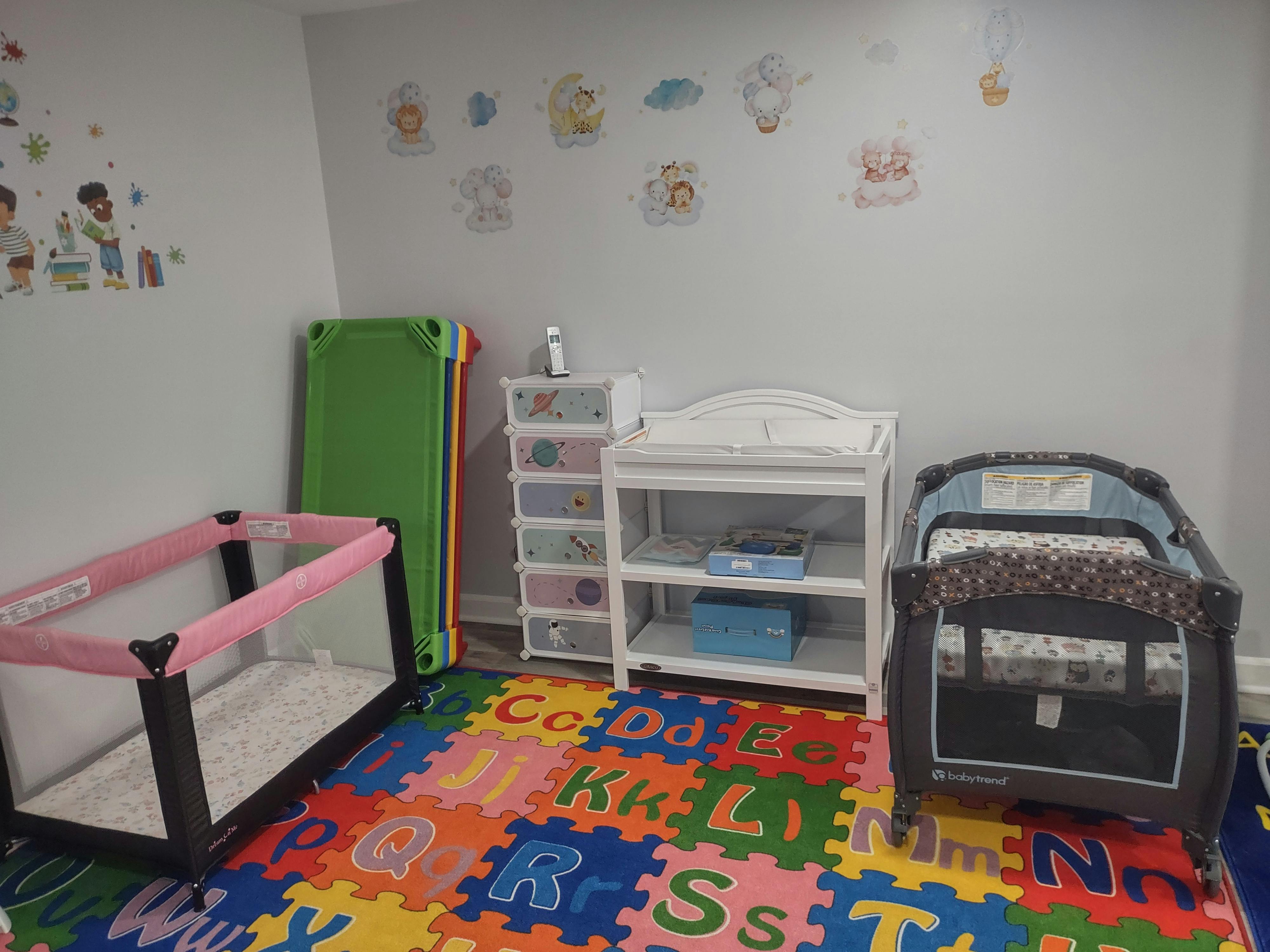Nursery room with two cribs, a changing table, and an alphabet mat on the floor