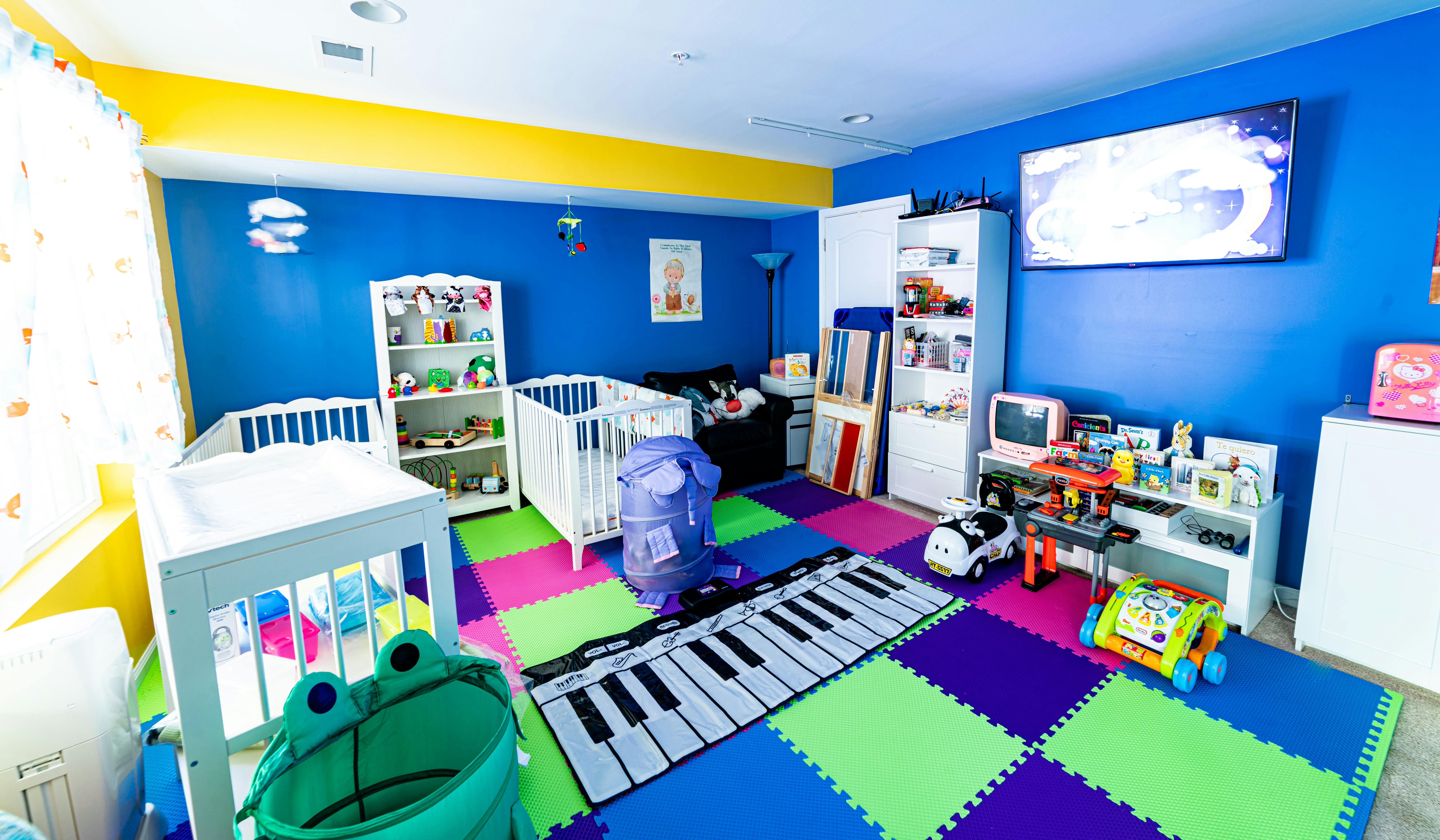 Nursery room with two cribs, colorful floor mats, and toys