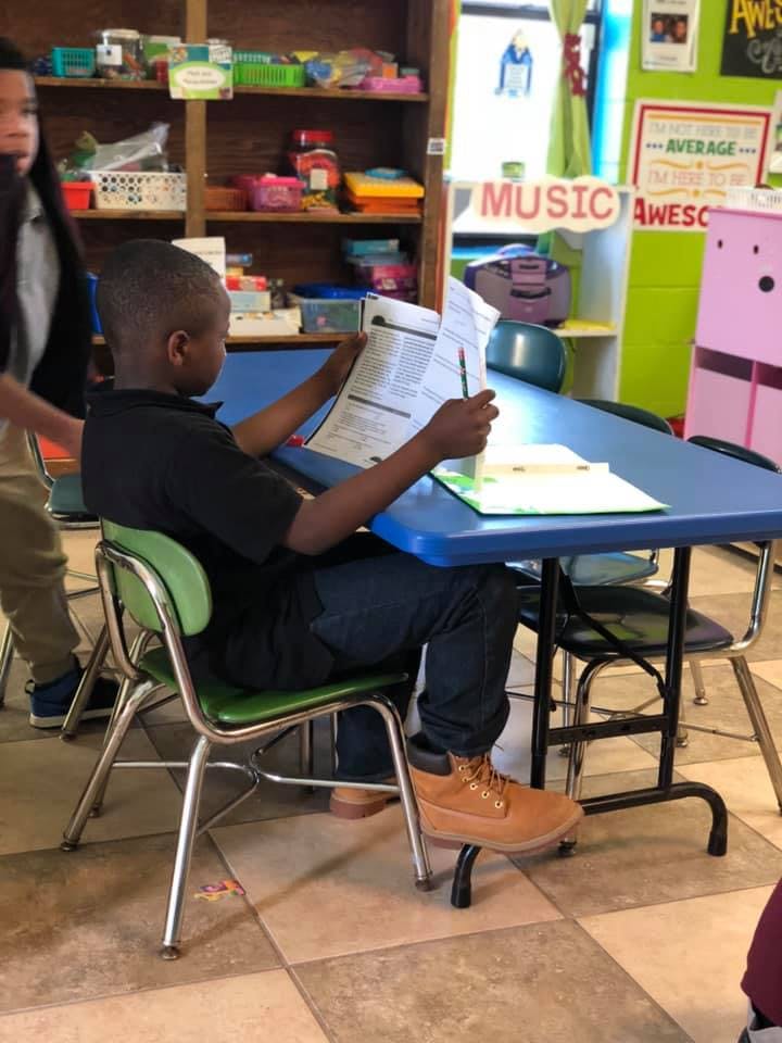 Child sitting at a table reading a paper in a classroom