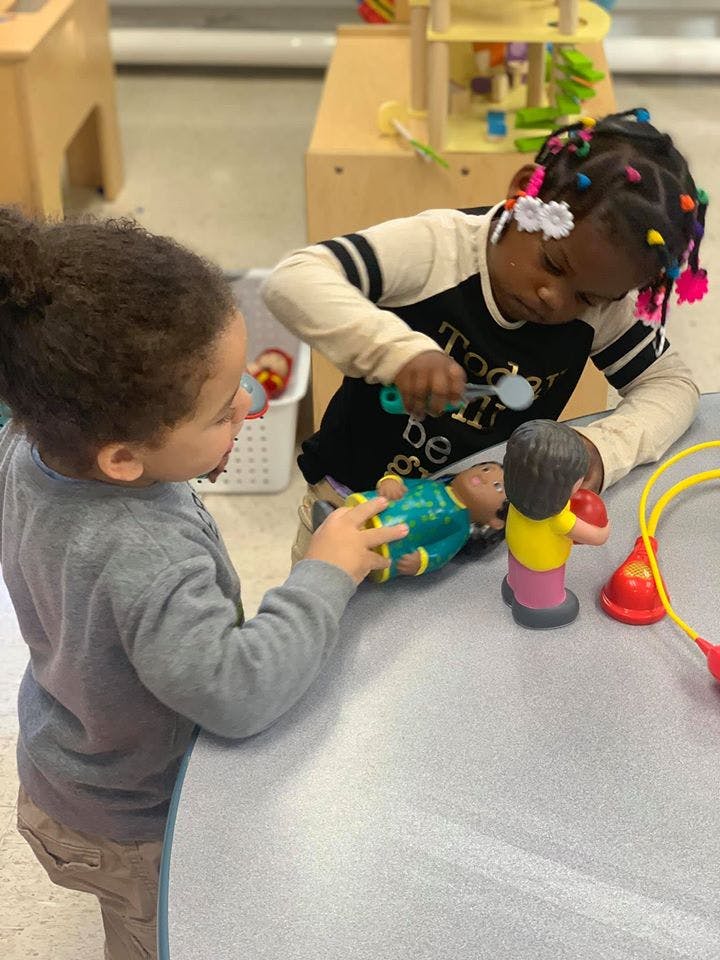 Two children playing with dolls and toy medical tools at a table