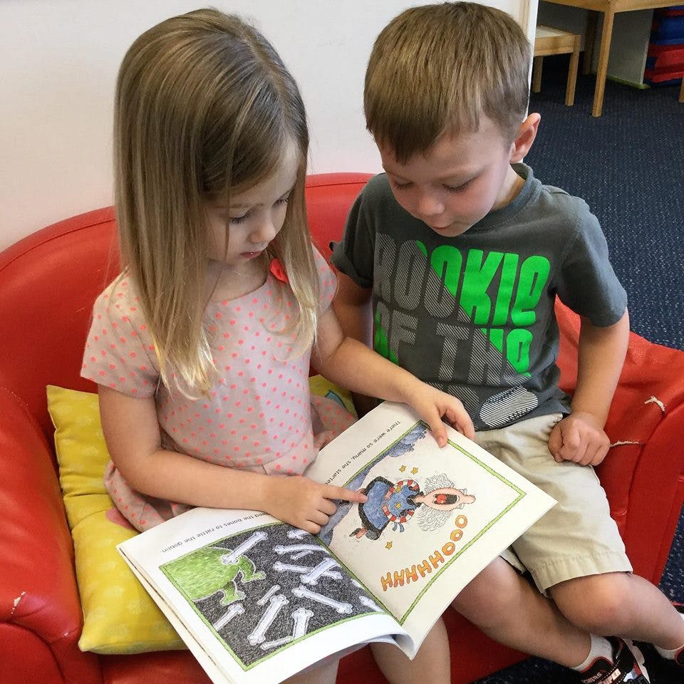 Two children sitting on a red couch reading a book together