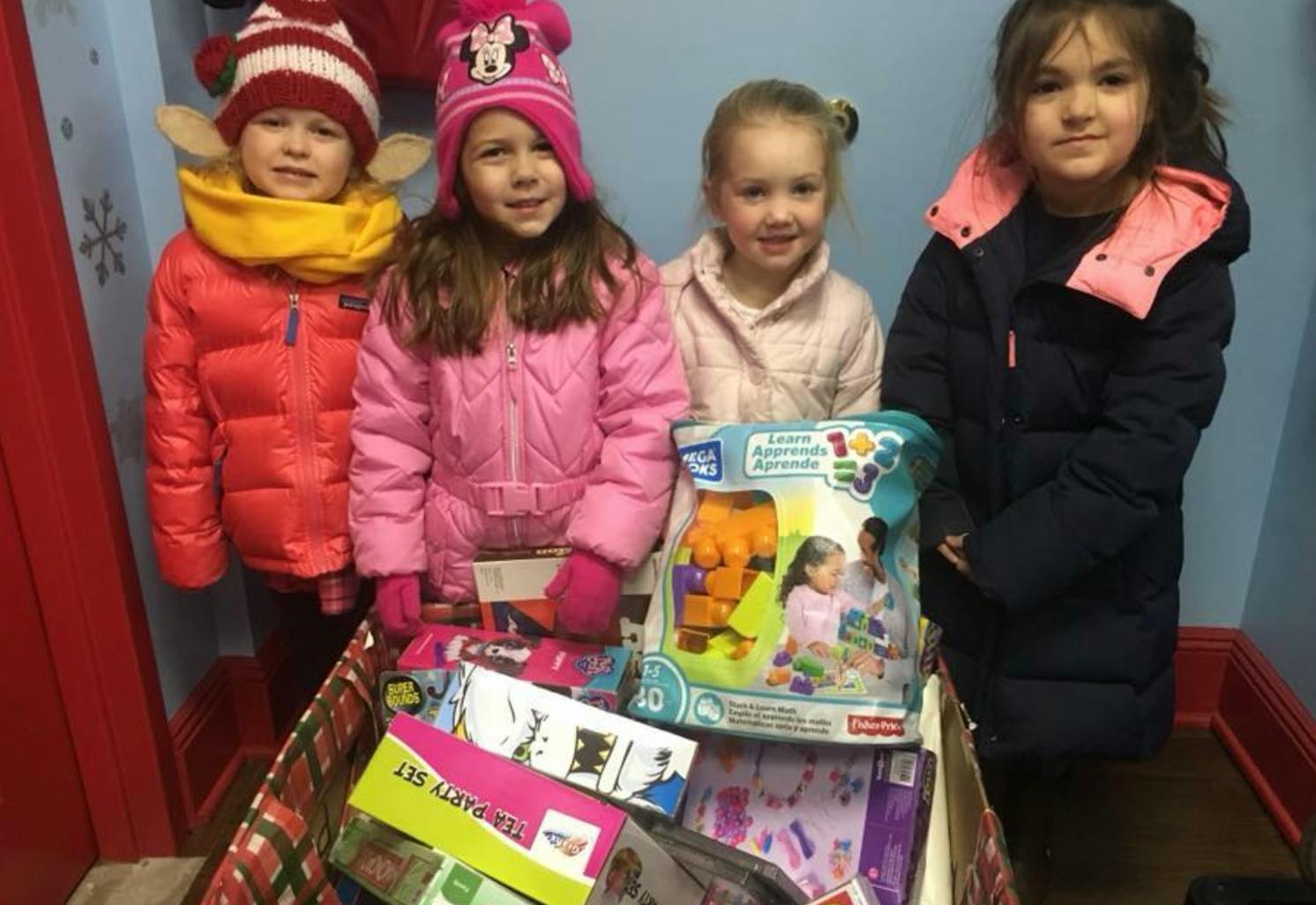 Four children standing behind a box of toys
