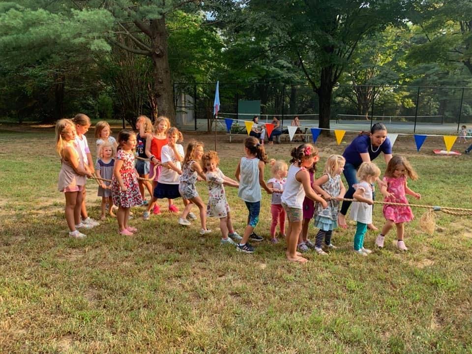 Children playing tug-of-war outdoors with an adult supervising