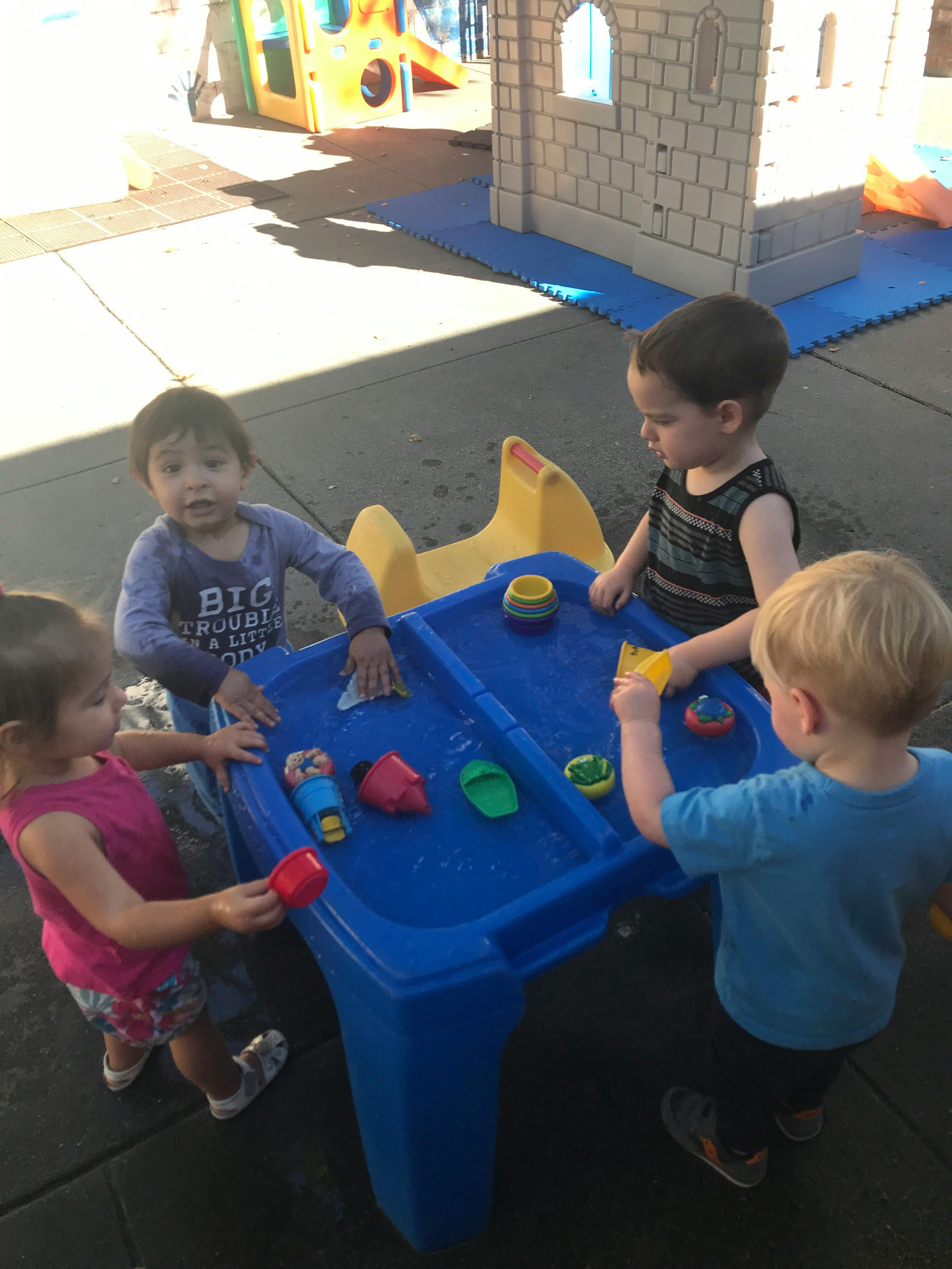 Four children playing at a blue water table outdoors