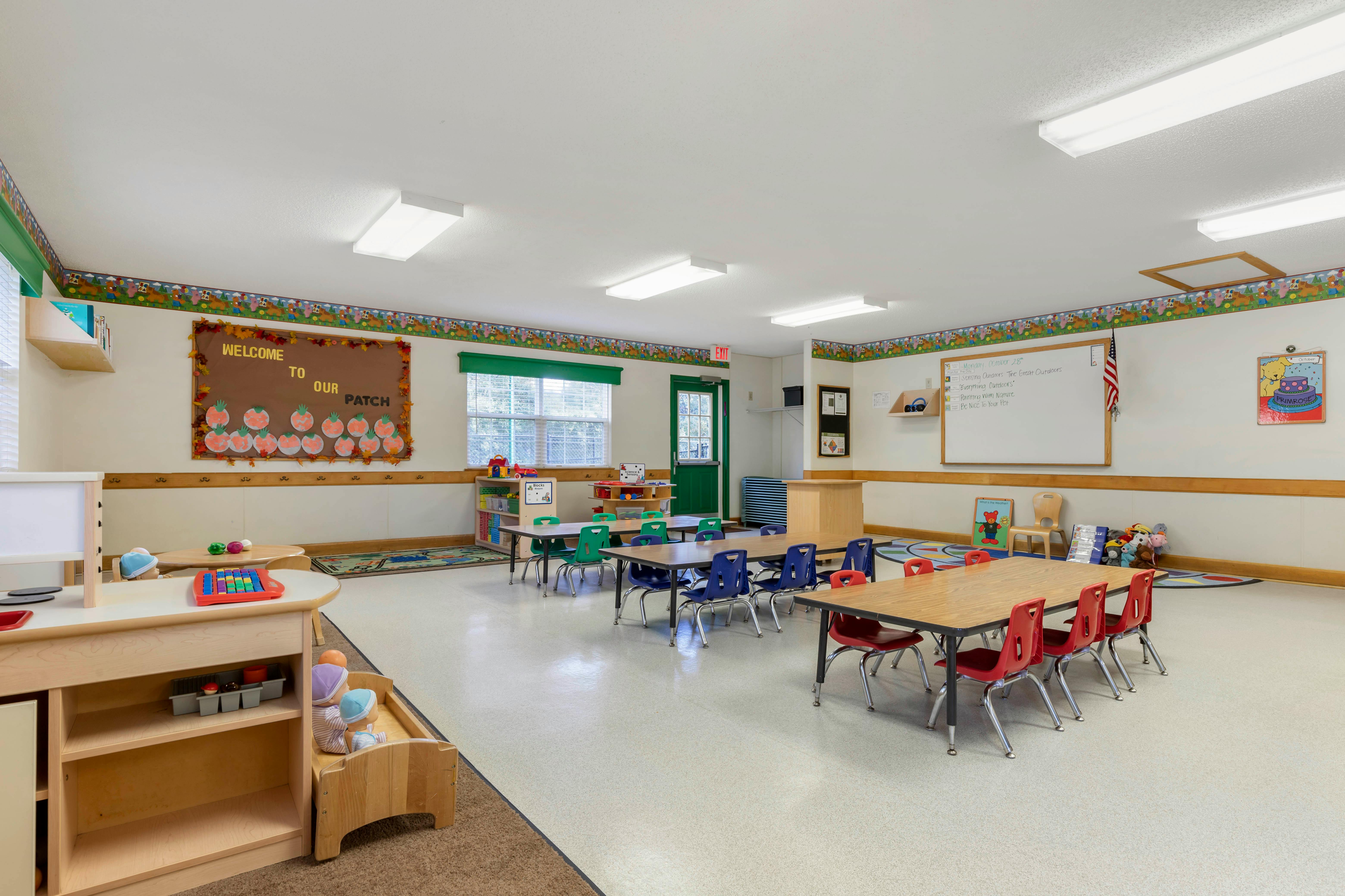 Classroom with small tables and chairs, a play kitchen, and a whiteboard