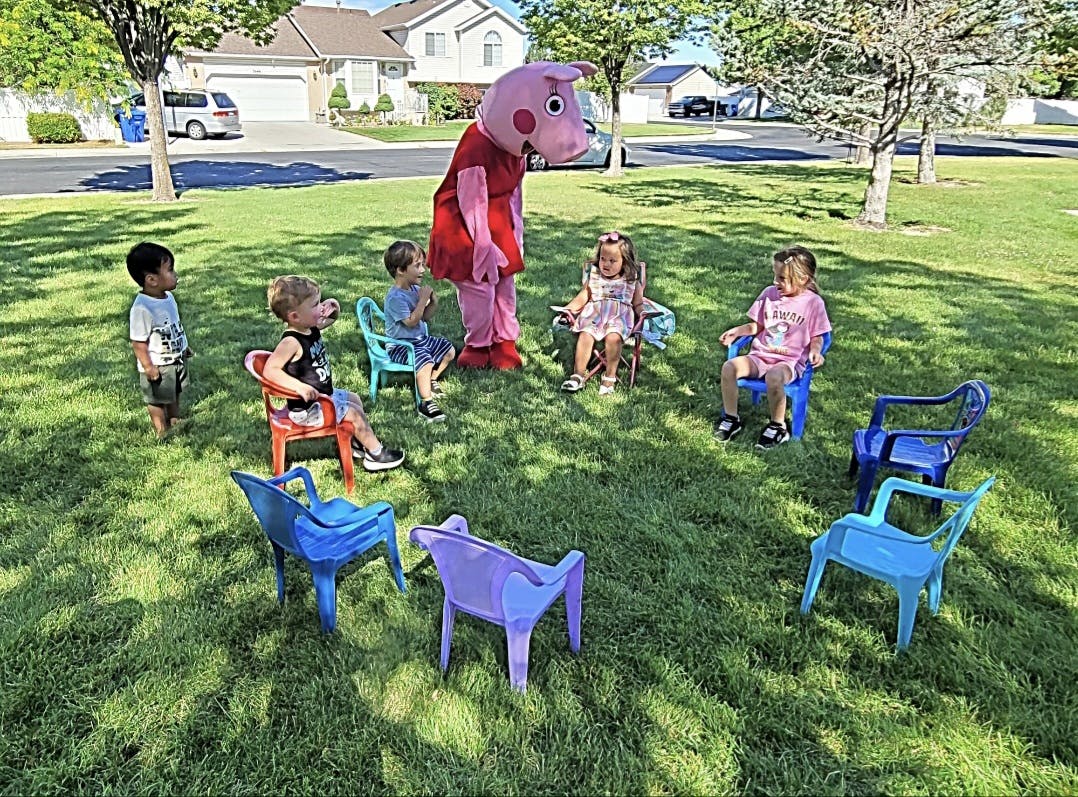Mascot pig standing with children seated in small chairs on grass