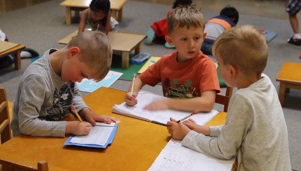 Three children writing at desks in a classroom