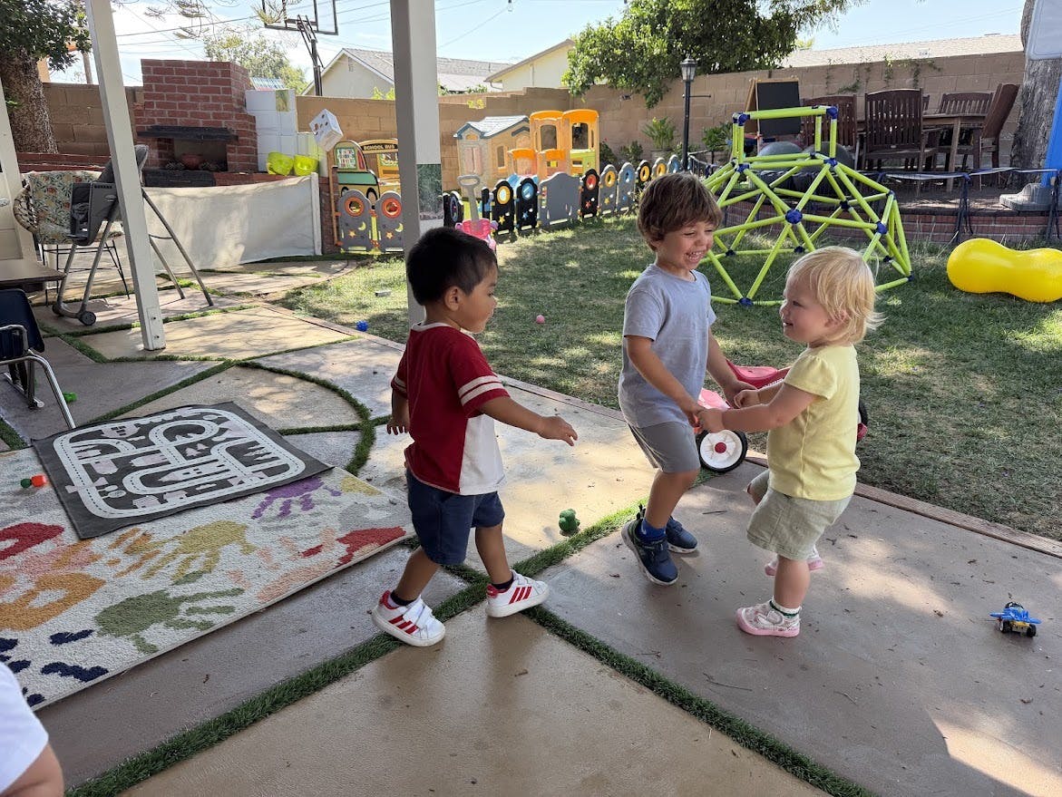 Three children playing and holding hands on a patio