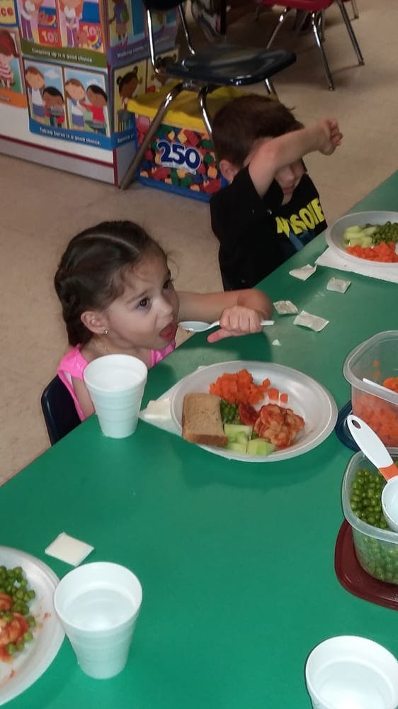 Child eating a meal at a table with another child in the background