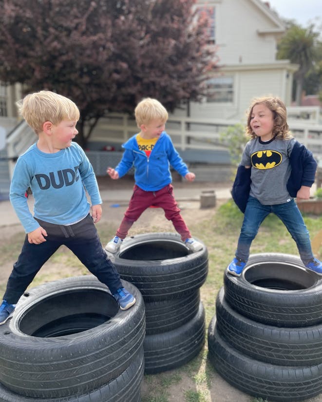 Three children standing on stacks of tires outdoors