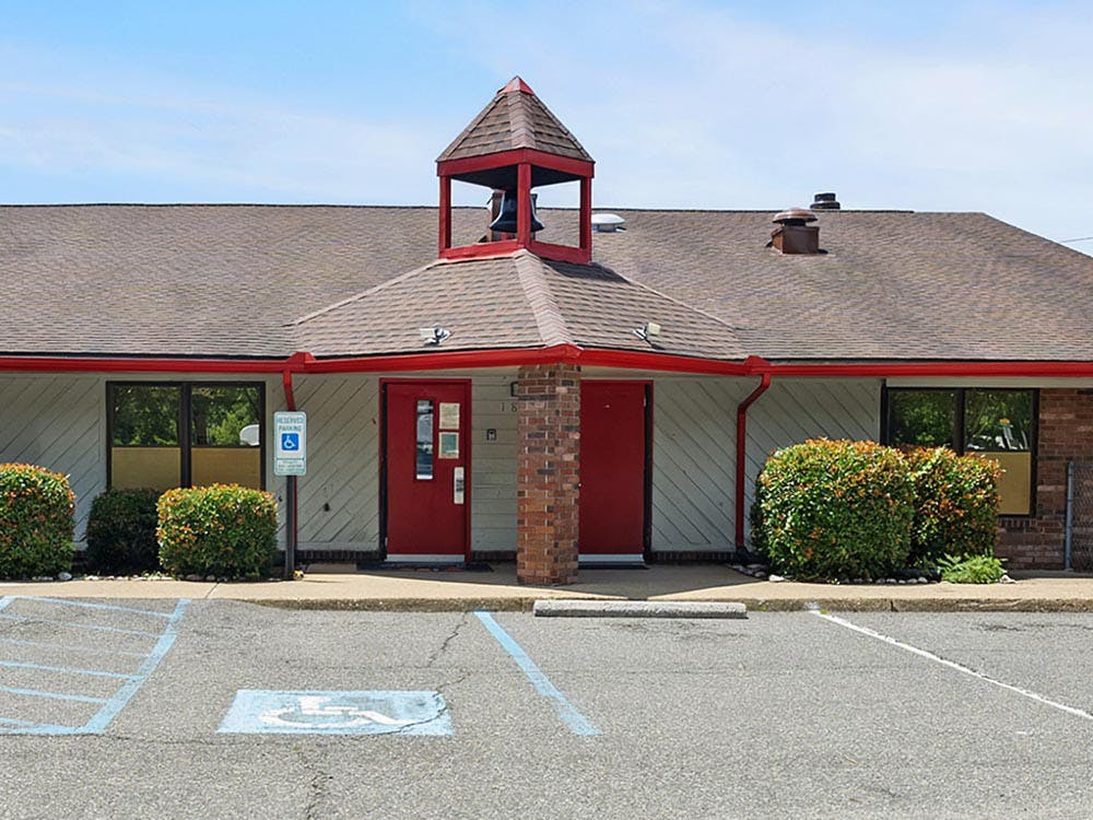 Front exterior of a building with red doors, a small bell tower, and accessible parking