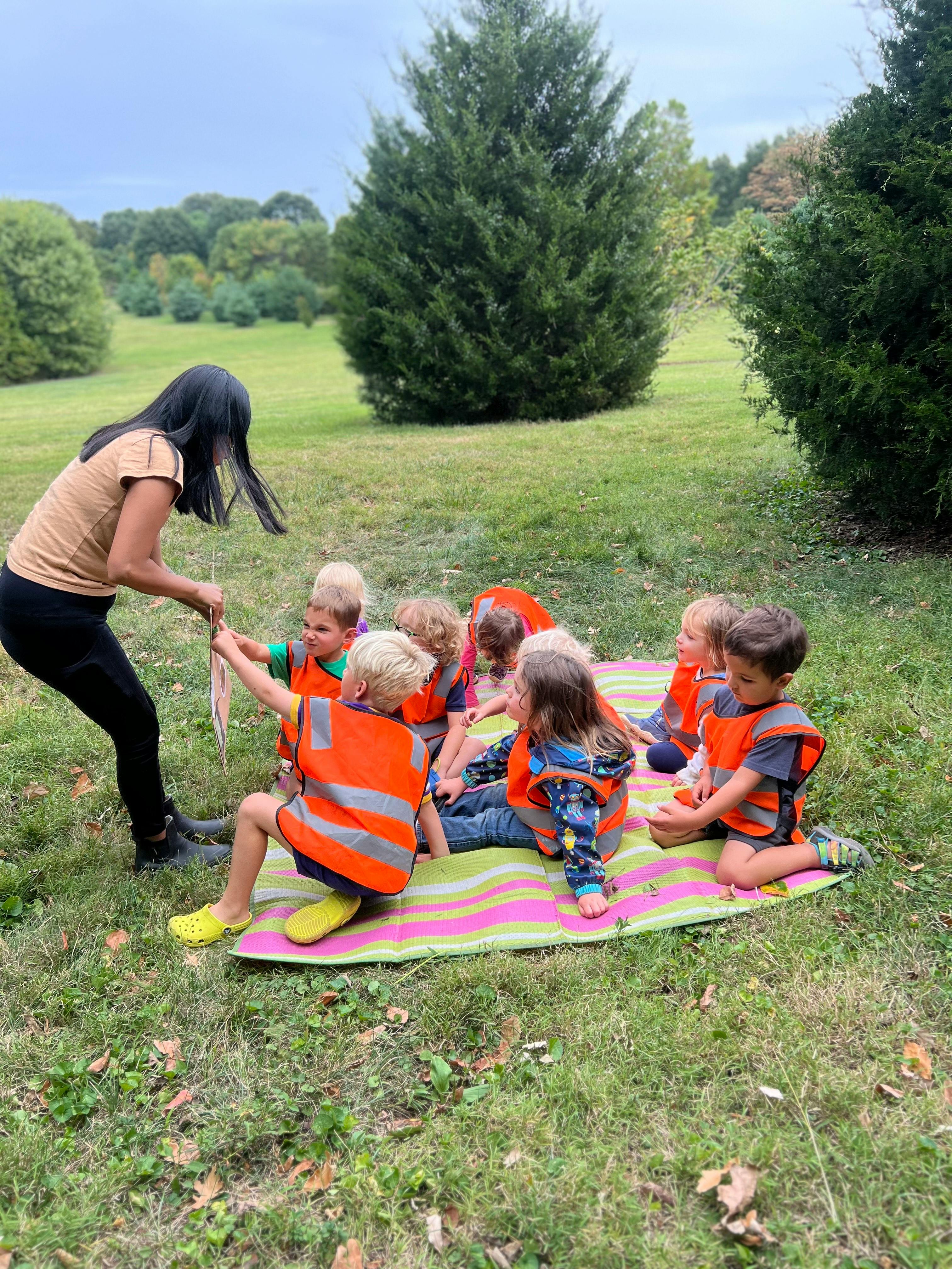 Adult and children in orange vests on a blanket outdoors
