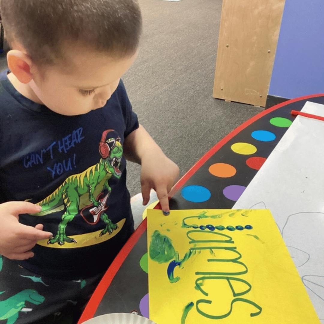 Child pointing at a yellow paper with the name "James" written on it