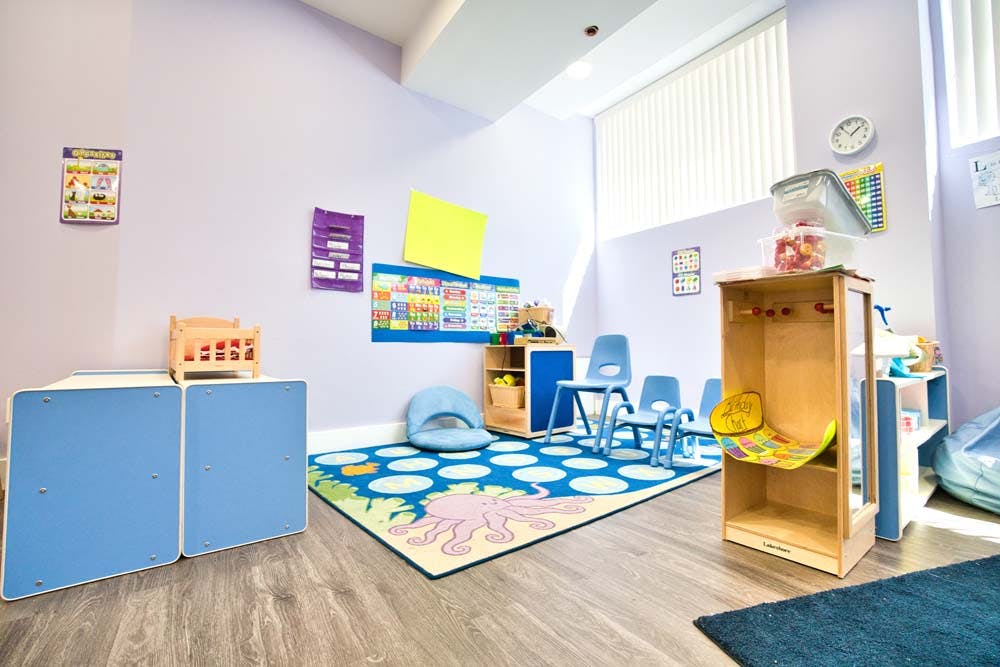 Children's classroom with small tables and chairs, colorful rug, and storage units