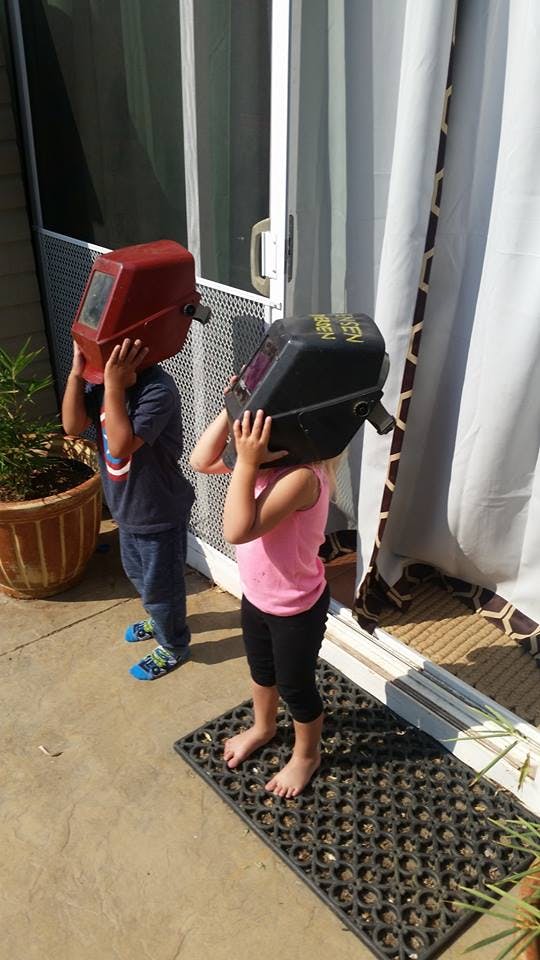Two children wearing welding helmets