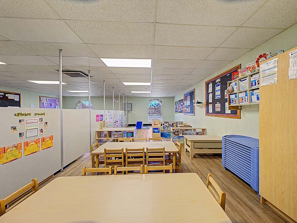 Empty classroom with small tables and chairs, partition walls, and bulletin boards