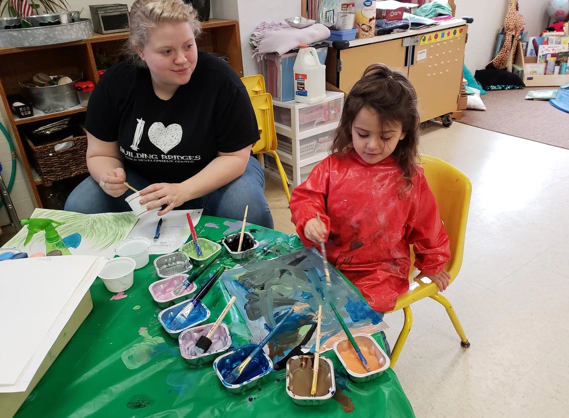 Adult and child painting at a table in a classroom