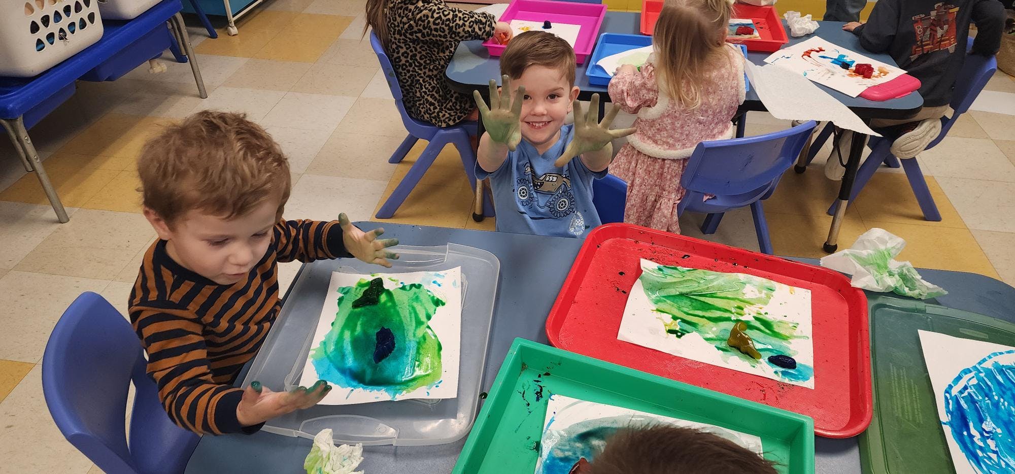 Children painting with their hands at tables in a classroom