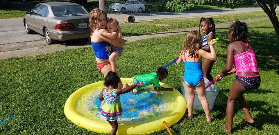 Children playing in and around a yellow inflatable pool in a grassy yard