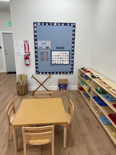 Classroom with a small wooden table and chairs, bulletin board, and shelves
