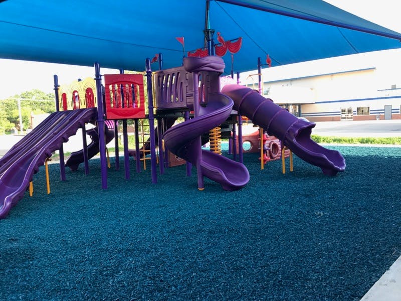 Playground with purple slides and blue ground covering under a blue canopy
